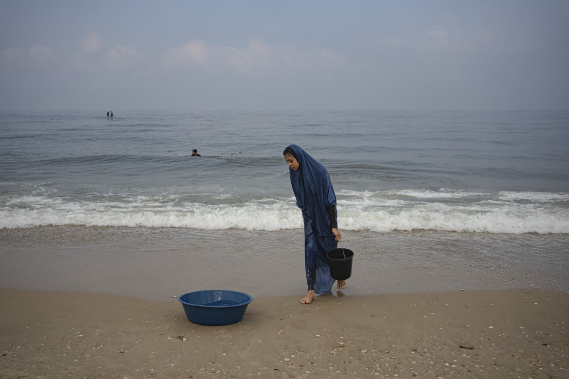 Una donna palestinese a Gaza raccoglie l'acqua di mare per il bucato, foto Fatima Shbair /Ap